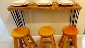 A kitchen area with a wooden countertop, three stools, and a set of plates and glasses.