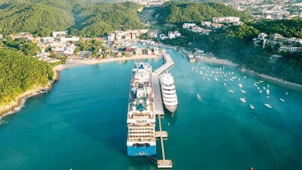 A cruise ship docked at a port with a marina and surrounding buildings.