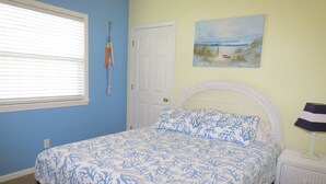 A bedroom with a bed, a door, a window, a painting, and a lamp.