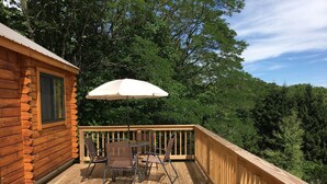 Een houten terras met een tafel, stoelen, een parasol en uitzicht op een bos.
