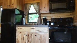Een keuken met houten kastjes, een koelkast, een magnetron, een fornuis en een raam met gordijnen.
