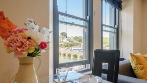 A dining table with a vase of flowers, plates, and glasses, overlooking a bridge and water. - 1 bedroom accommodation in Looe (Looe)