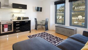 A modern kitchen with a dining area, a large window with a view of a harbor, and a cozy seating area with a patterned rug. - 1 bedroom accommodation in Looe (Looe)