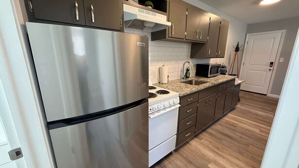 A modern kitchen with stainless steel appliances, a microwave, and wooden flooring. - Lakeside Serenity: Charming One-Bedroom Villa (Bridgman)
