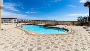 En swimmingpool med ett kaklat poolområde, solstolar och en trädeckad yta.