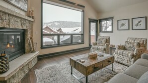 A spacious living room with a stone fireplace, large windows, and a cozy seating area. - Alders 46 Outpost Dr (Keystone)