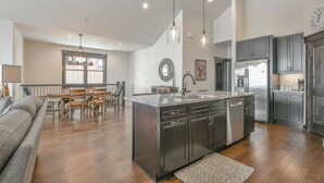 A spacious kitchen with dark cabinetry, a large island, and a dining area with wooden chairs and a table. - Alders 46 Outpost Dr (Keystone)