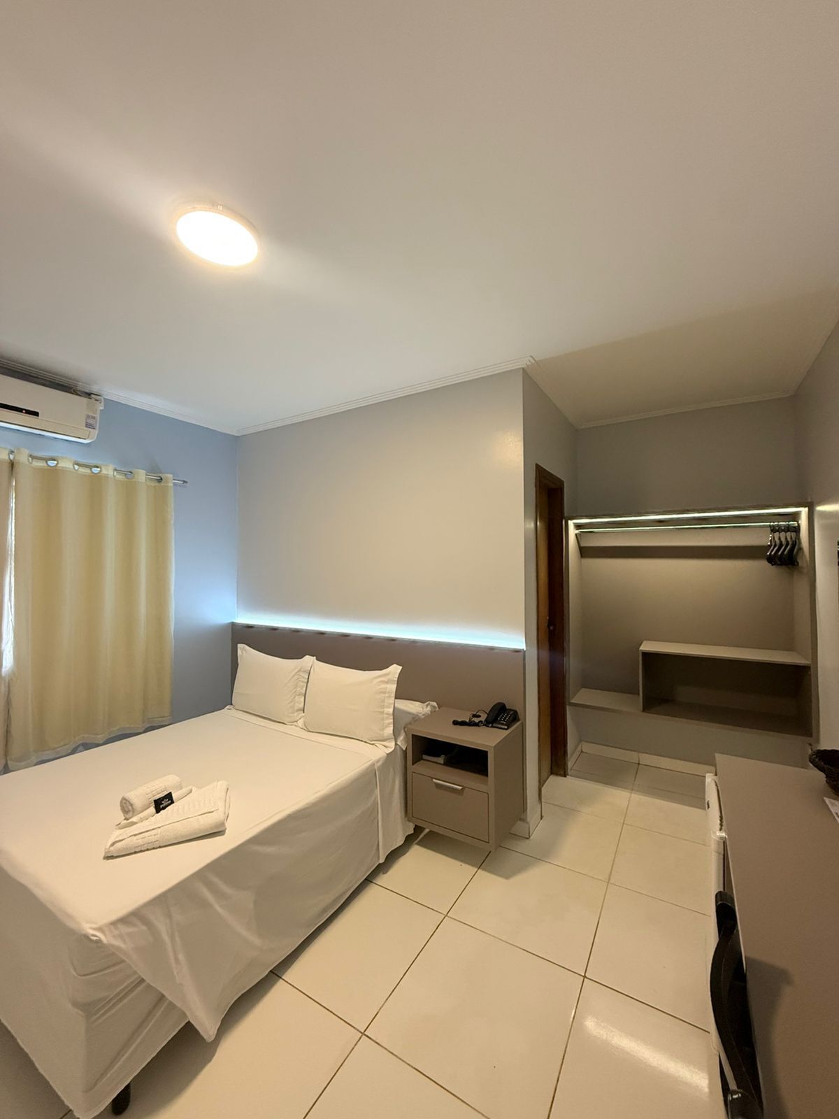 A hotel room with a bed, bedside table, and a desk with a chair.