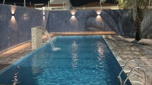 Una piscina rettangolare con elemento d'acqua, circondata da un muro in pietra con luci integrate.
