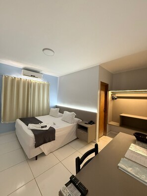 Una habitación de hotel con cama, mesita de noche, escritorio, silla y aire acondicionado.