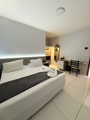 Habitación de hotel con una cama grande, un escritorio, una silla, un espejo y una pequeña kitchenette.