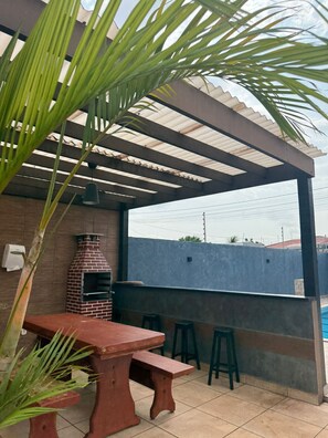Un patio al aire libre con un horno de pizza de ladrillo, una mesa de madera y taburetes de bar.