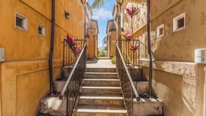 Un estrecho callejón con una escalera que conduce a la entrada de un edificio, flanqueado por paredes amarillas y pequeñas ventanas.