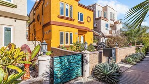 Un edificio residencial con fachada amarilla, entrada protegida por una reja y un jardín bien cuidado con diversas plantas.
