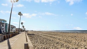 Una playa con paseo marítimo de hormigón, palmeras y edificios a lo largo de la costa.