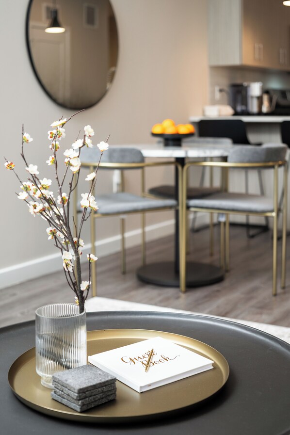 A dining area with a round table, chairs, a vase with flowers, a tray with a glass, and a menu.