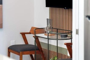 Un comedor moderno con una silla de madera y una mesa de vidrio, un televisor montado en la pared y un panel de madera vertical.