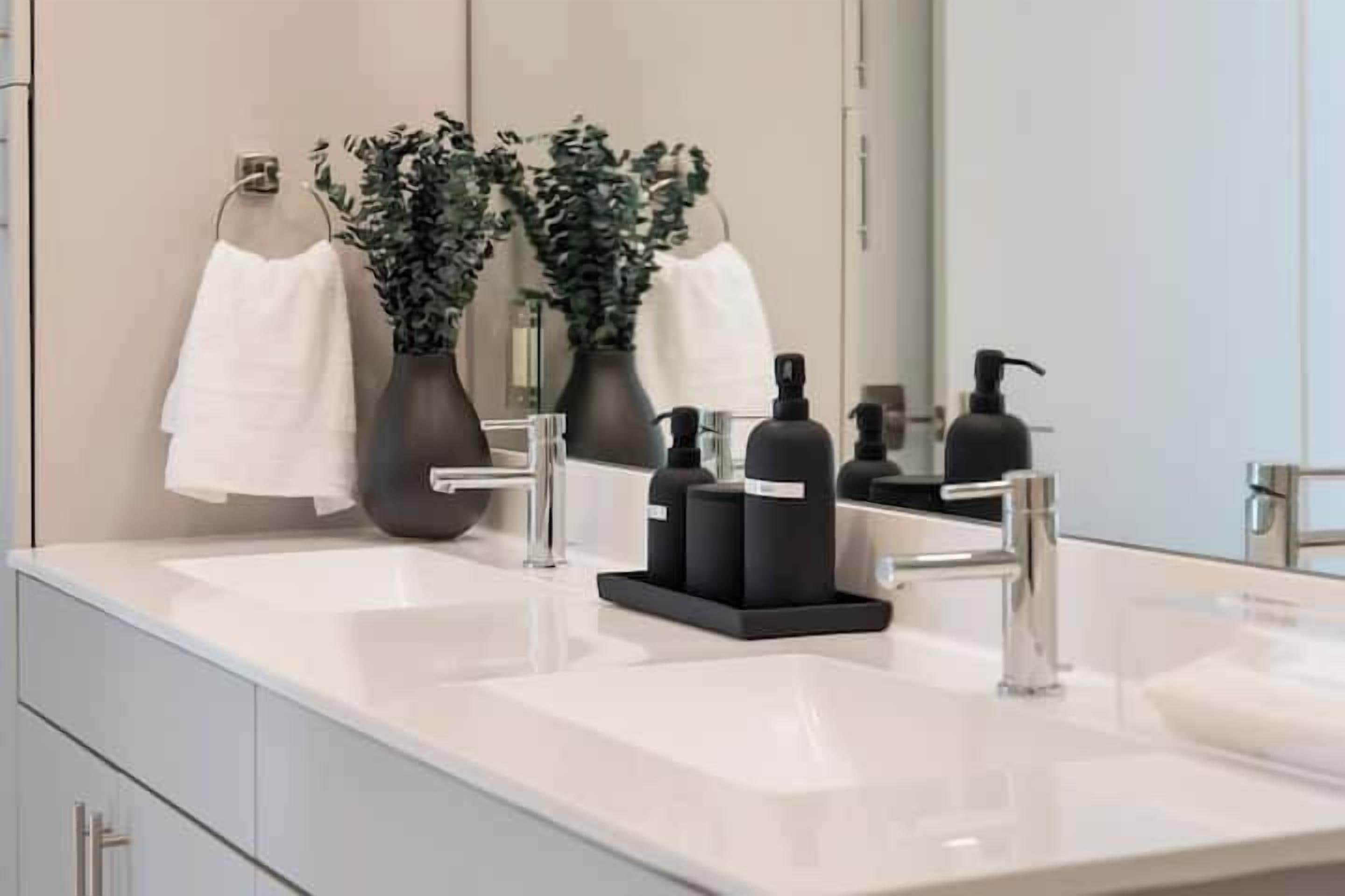 A modern bathroom with two sinks, a large mirror, and decorative vases.