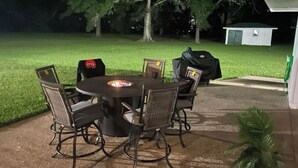 An outdoor patio with a round table and six chairs, surrounded by a grassy area and trees. - "WELCOME TO ARTHUR’S PLACE! IDEAL FOR LARGE GROUPS AND PET FRIENDLY."  (Baton Rouge)