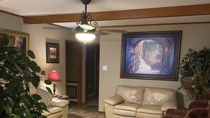 A living room with a beige sofa, a patterned armchair, a red lamp, and a large framed picture on the wall. - "WELCOME TO ARTHUR’S PLACE! IDEAL FOR LARGE GROUPS AND PET FRIENDLY."  (Baton Rouge)