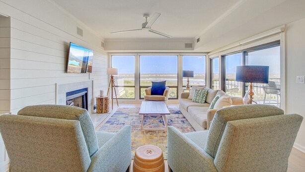 Un amplio salón con chimenea, ventanas grandes y vista al océano.
