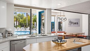 Una cocina moderna con una isla grande, vista a una piscina y un comedor con vistas al exterior.