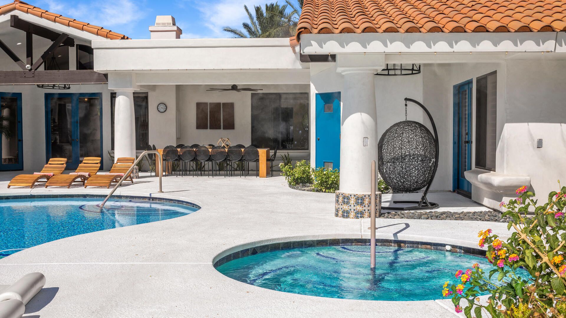 A pool area with two swimming pools, lounge chairs, a table with chairs, and a decorative spherical object.