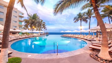 Una piscina de resort con sillones de descanso y palmeras.