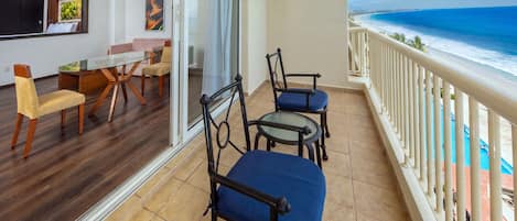 A balcony with a view of the ocean, furnished with two chairs and a table.