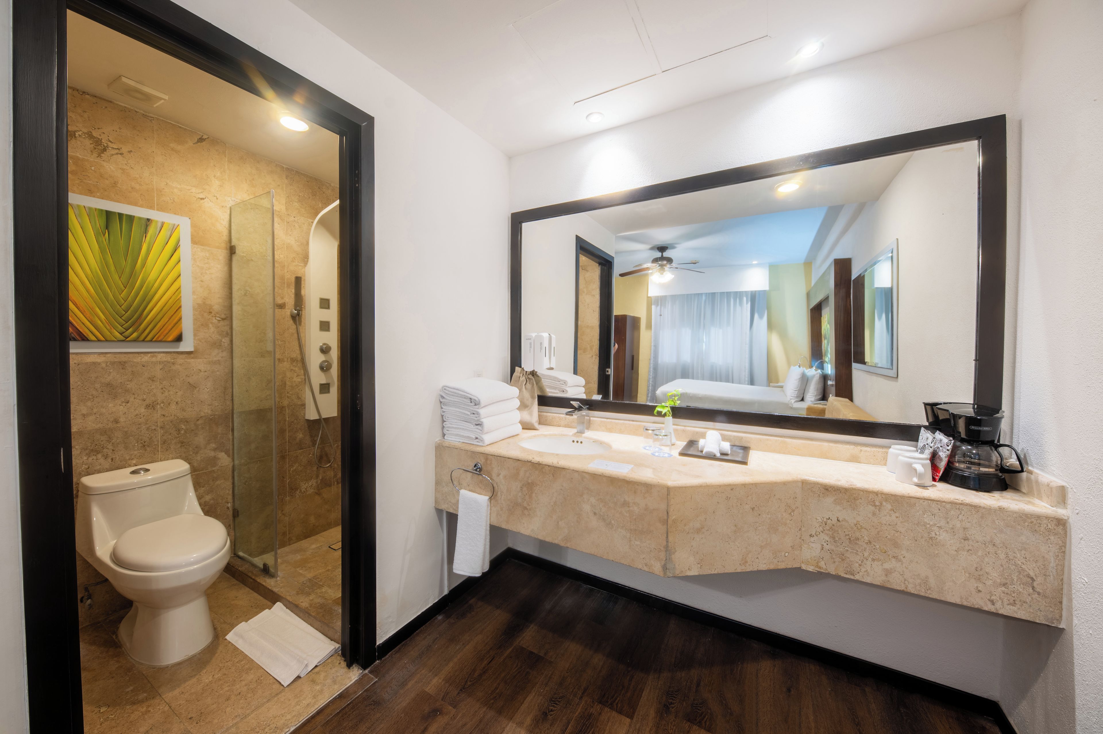 A hotel bathroom with a shower, toilet, sink, and a large mirror.
