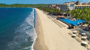 Un resort en la playa con piscina, tumbonas y vistas al océano.