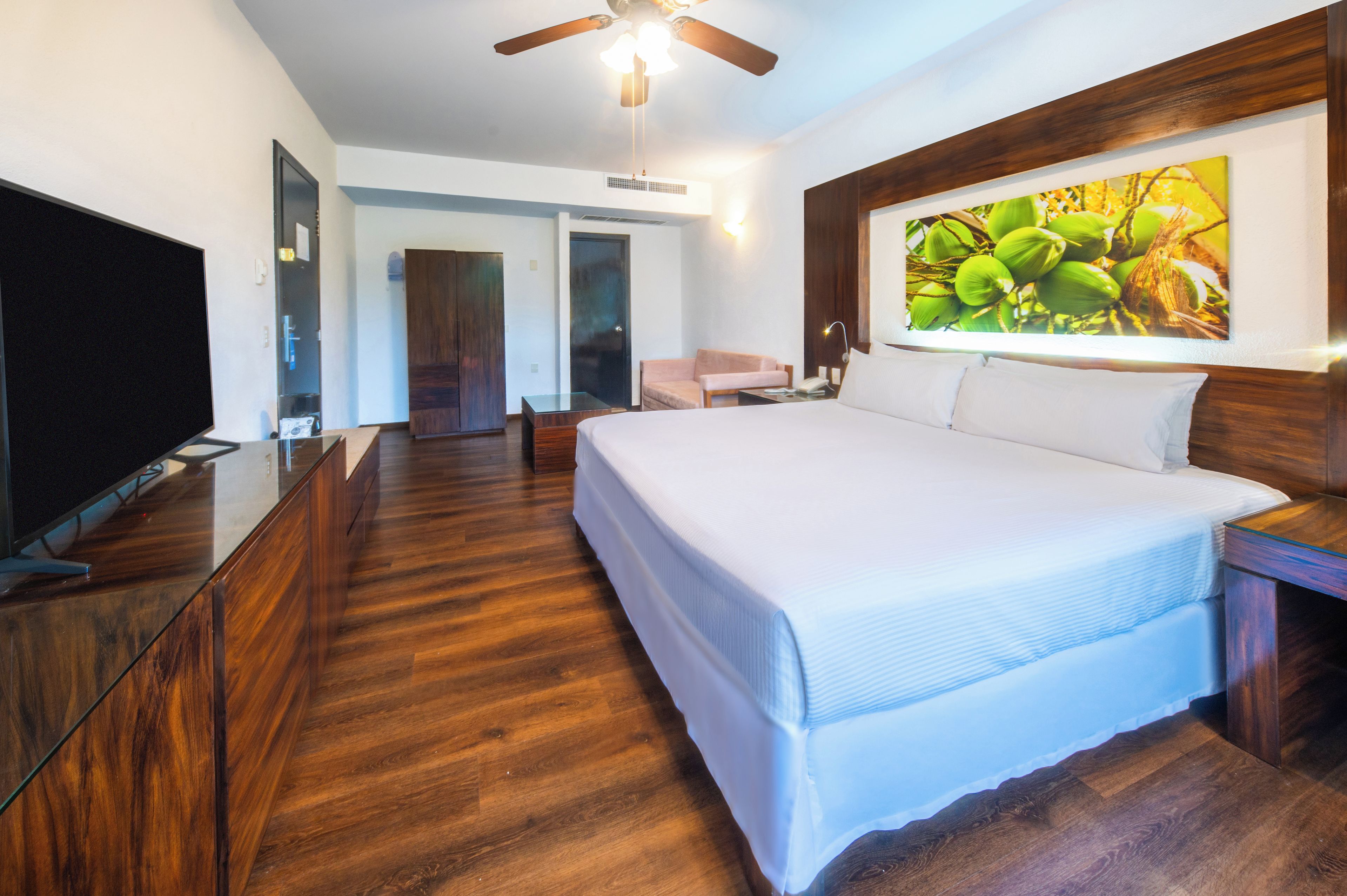 A hotel room with a large bed, a television, a desk, and a painting on the wall.