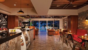 Un moderno vestíbulo de hotel con una barra de café, zona de estar y vistas a la piscina.