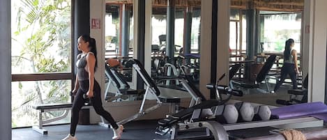 Een sportschool met trainingsapparatuur, grote ramen en een rieten dakconstructie.