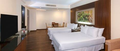A hotel room with two beds, a television, a dining table with chairs, and a painting on the wall.