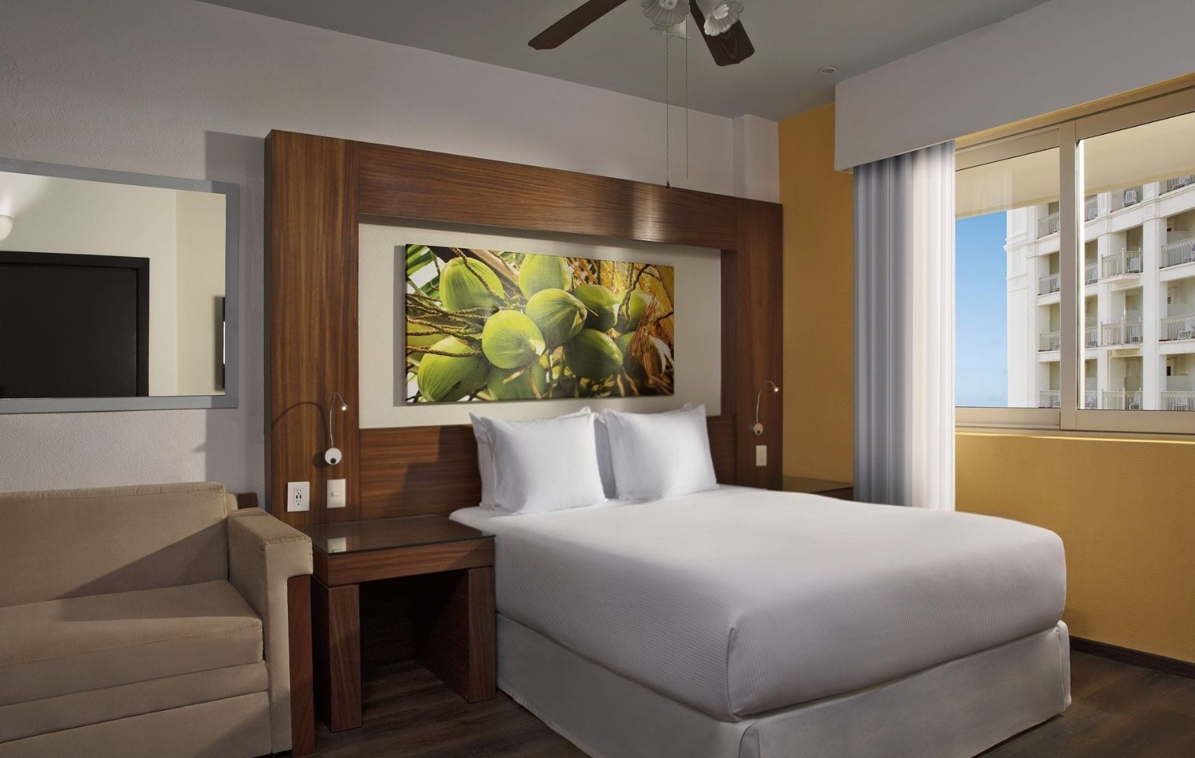 A hotel room with a bed, a nightstand, a chair, a painting, and a window with a view of a building.