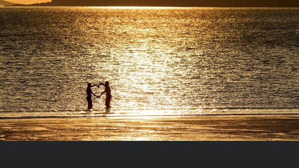 Un coucher de soleil sur une étendue d’eau, avec les silhouettes de personnes se tenant la main.