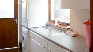 Une cuisine de taille réduite équipée d’un lave-linge, d’un évier et d’une fenêtre.
