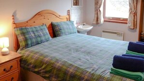 Une chambre à coucher avec un lit en bois, une literie à carreaux, une table de chevet avec une lampe, un lavabo et une fenêtre avec des rideaux.