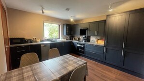 Une cuisine moderne avec des meubles de couleur sombre, un four à micro-ondes, un évier et un coin repas comprenant une table et des chaises.