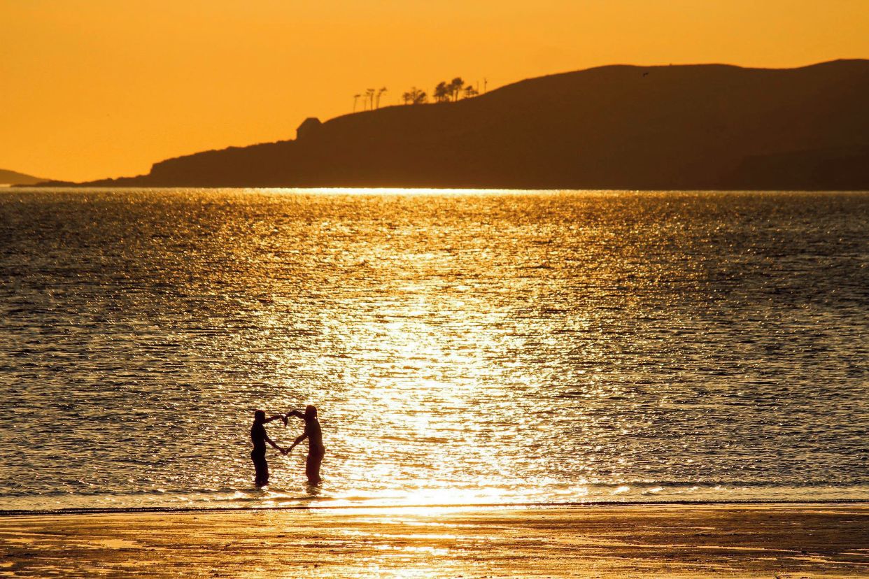 A sunset over a body of water with silhouettes of people holding hands.