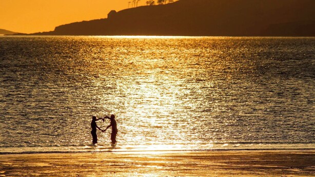Tramonto su uno specchio d'acqua con sagome di persone che si tengono per mano.