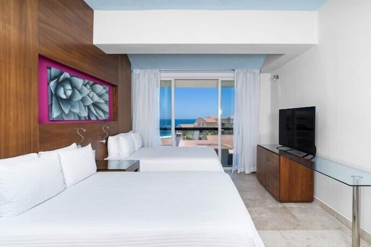 Ein Hotelzimmer mit zwei Betten, einem Fernseher und einem Balkon mit Meerblick.