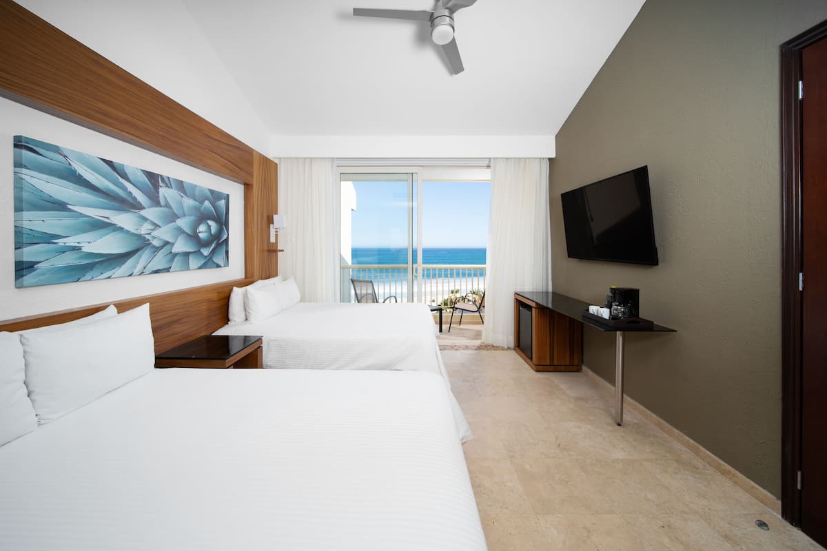 Ein Hotelzimmer mit zwei Betten, einem Deckenventilator, einem Fernseher und einem Balkon mit Meerblick.