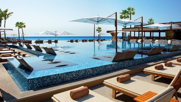 Un espace aménagé au bord de la piscine, avec des chaises longues et des parasols, offrant une vue dégagée sur l’océan, et une piscine carrelée.