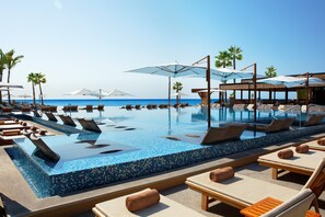 Un área al borde de la piscina con sillones de descanso y sombrillas, con vista despejada al océano y una piscina con azulejos.