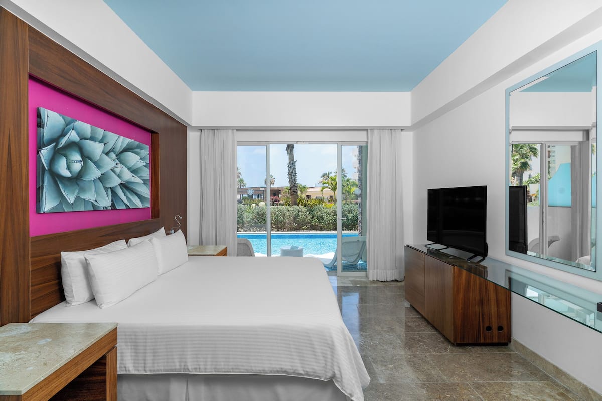 Ein Hotelzimmer mit einem großen Bett, einem Fernseher, einer Glasvitrine und Blick auf einen Swimmingpool.