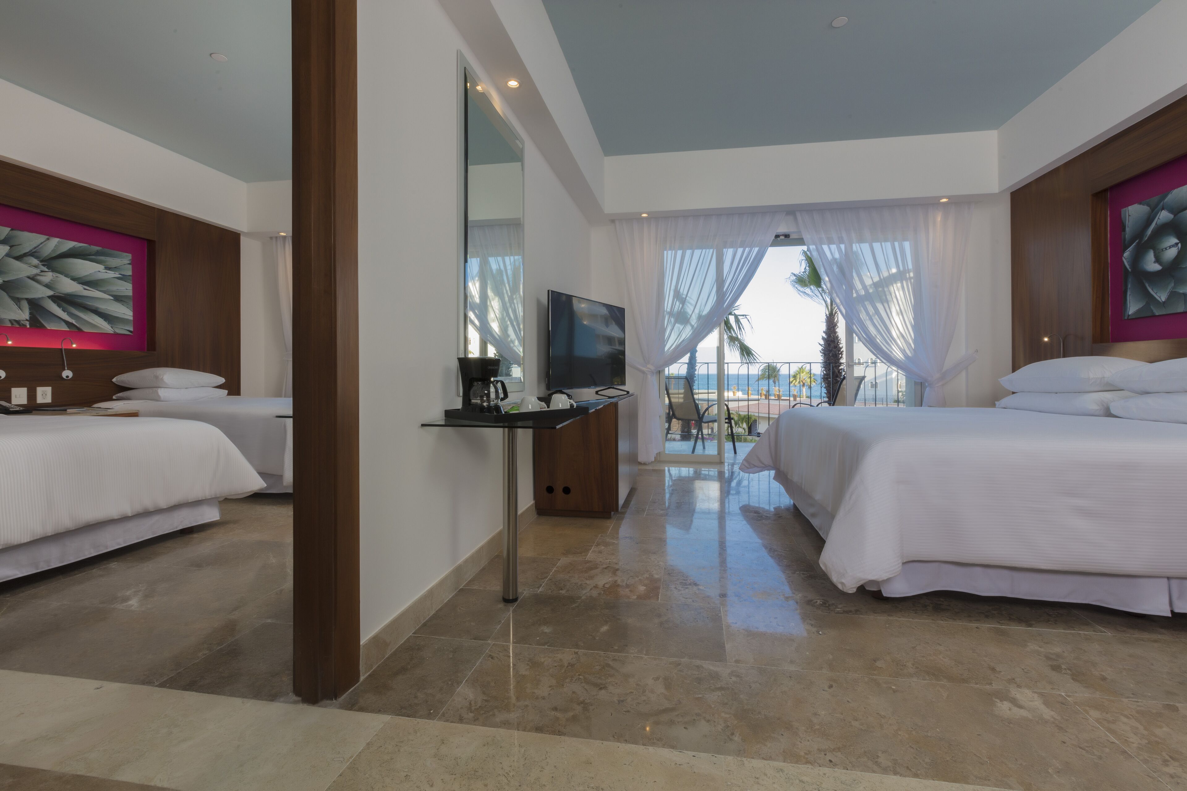 Habitación de hotel con dos camas, un escritorio con televisor y vista al océano.