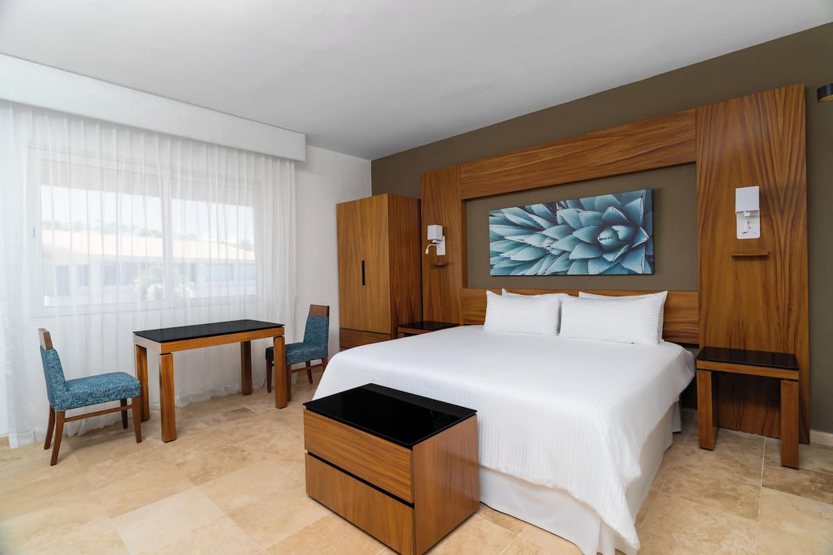 Ein Hotelzimmer mit einem großen Bett, einem Schreibtisch, einem Stuhl und einem Holzschrank.