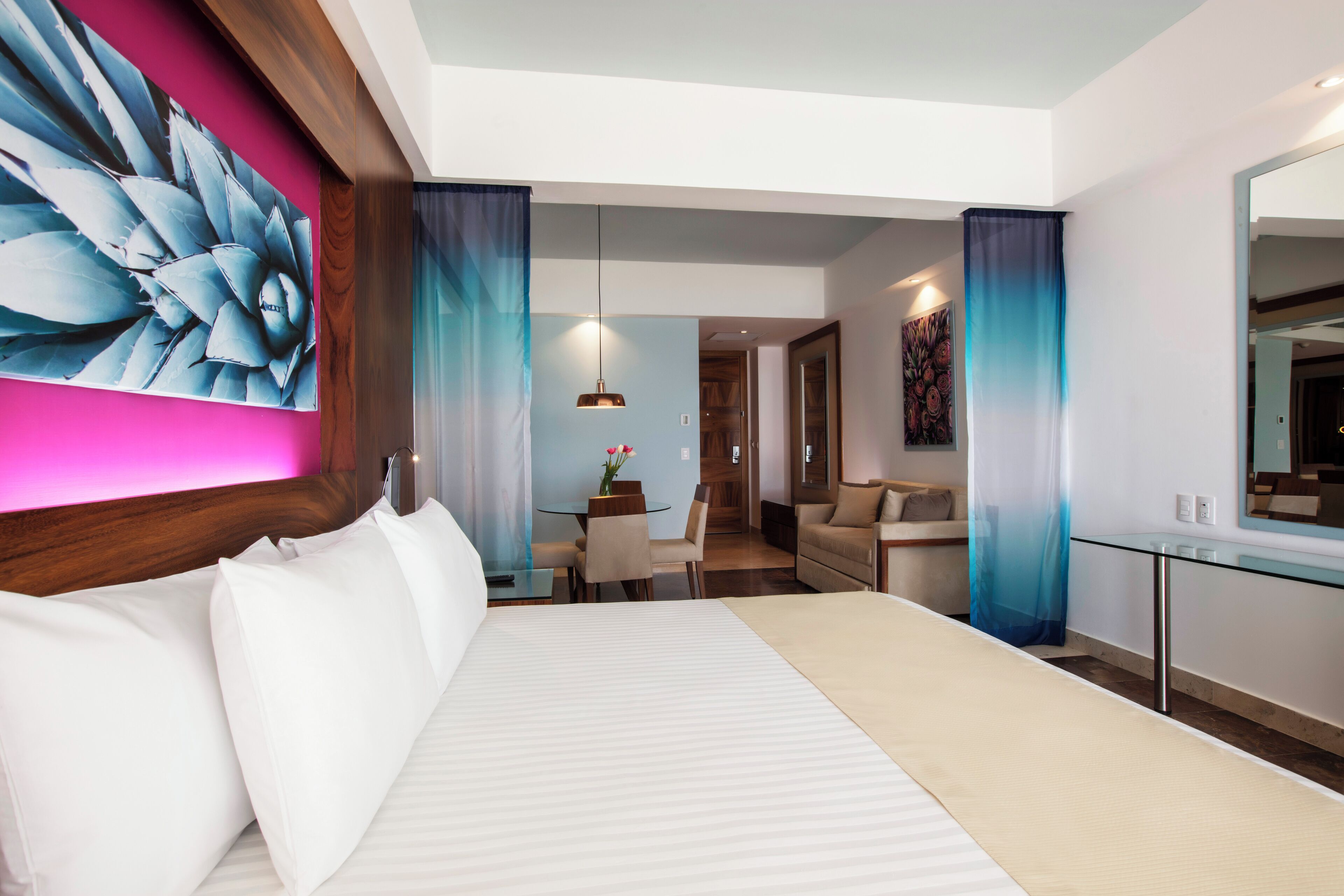 A modern hotel room with a large bed, a dining area, and a living space.